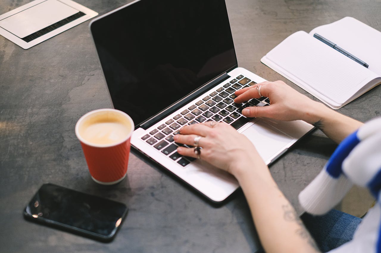 The Art of Drawing Readers In: Your attractive post title goes here A freelancer typing on a laptop with a cup of coffee, smartphone, and notepad on the table.